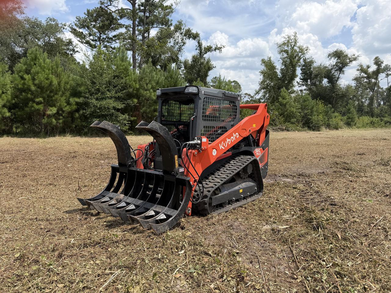 Kubota SVL 75-3 track loader fitted with a root grapple, parked on freshly cleared ground